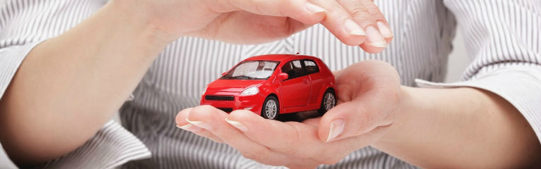 Mãos envolvem de forma protetora a miniatura de um carro vermelho.