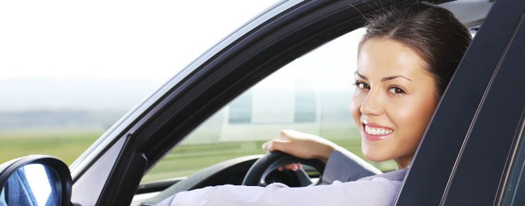 Mulher sentada no banco do motorista de um carro sorri enquanto olha para a câmera.