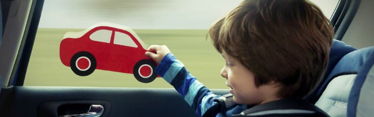 Criança sentada em cadeirinha brinca no banco traseiro de um carro.