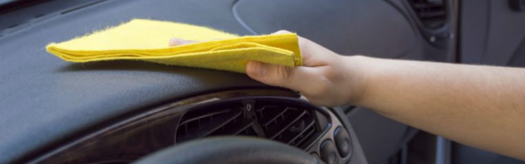 Pessoa utiliza uma flanela amarela para limpar o painel de um carro.