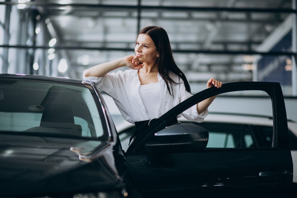 Imagem de uma mulher apoiada no carro com a porta aberta dentro de uma concessionária