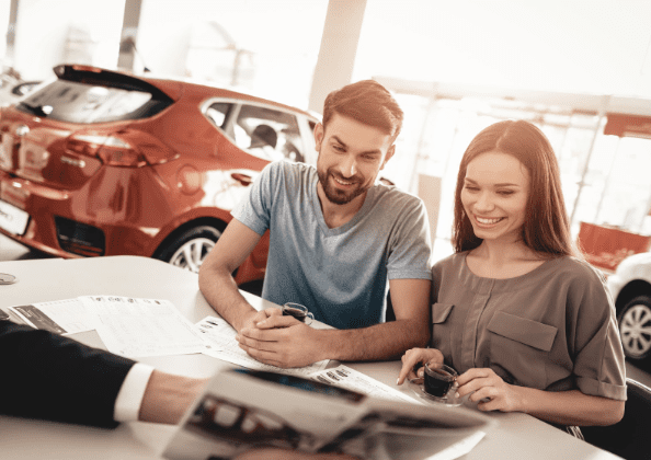 Homem e mulher sorrindo olhando catálogo de carros dentro de uma locadora.