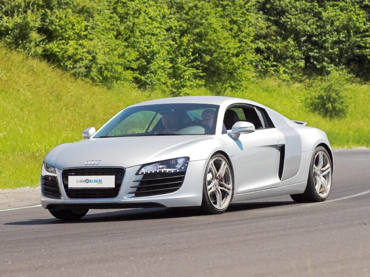 Audi R8 (2007) na cor prata em estrada com vegetação ao fundo.