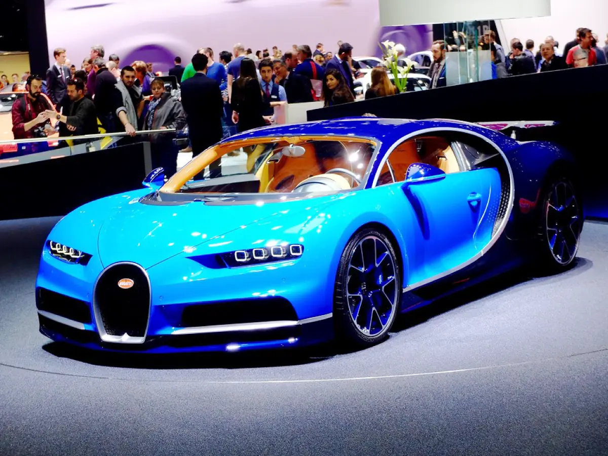 Bugatti Chiron (2016) na cor azul em exibição numa feira de automóvel com várias pessoas ao fundo admirando o carro.