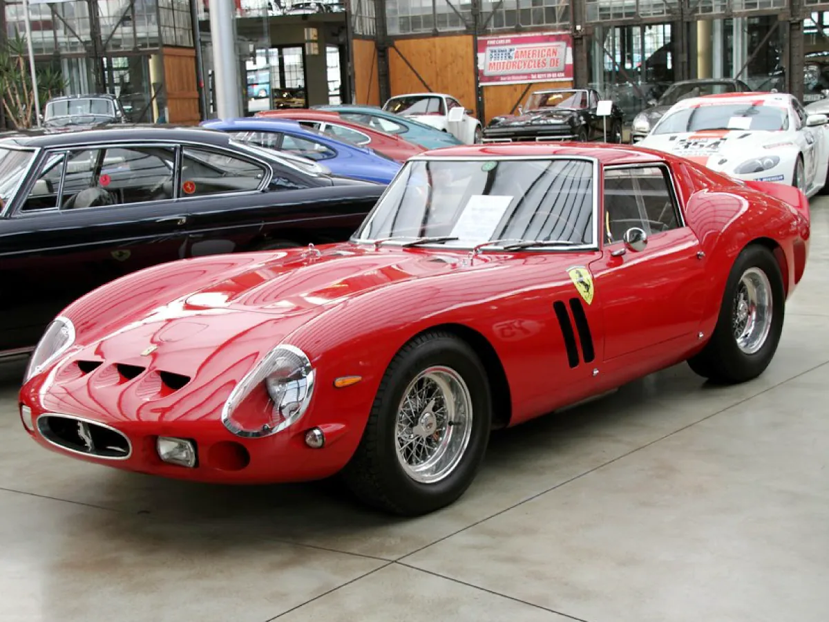 Ferrari 250 GTO (1962) na cor vermelha, estacionado em área externa ao lado de outros carros.