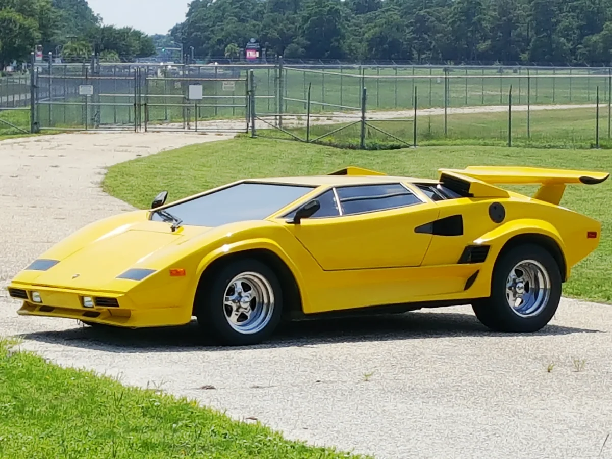 Lamborghini Countach (1974) na cor amarela estacionado de forma a fechar uma rua com portões e grades de ferro ao fundo.