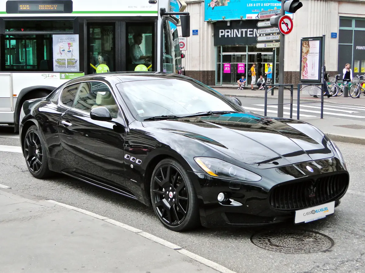 Maserati Gran-Turismo (2007) na cor preta aguardando no semáforo, com ônibus manobrando ao fundo e pessoas do outro lado da rua admirando o carro.