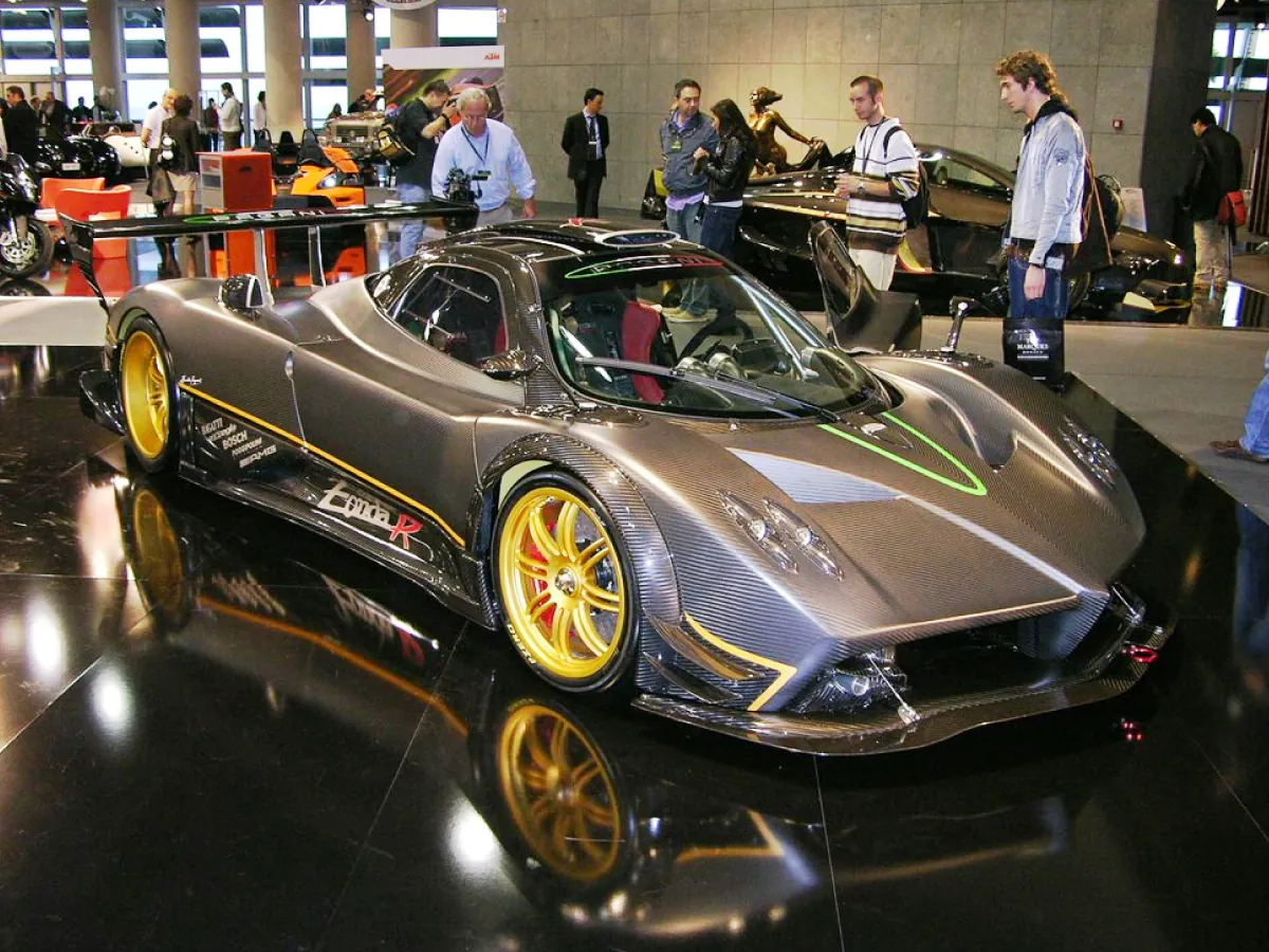 Automóvel Pagani Zonda R (2009), na cor cinza, em exposição sobre piso escuro e brilhoso, com pessoas ao redor admirando, filmando e fotografando o carro.