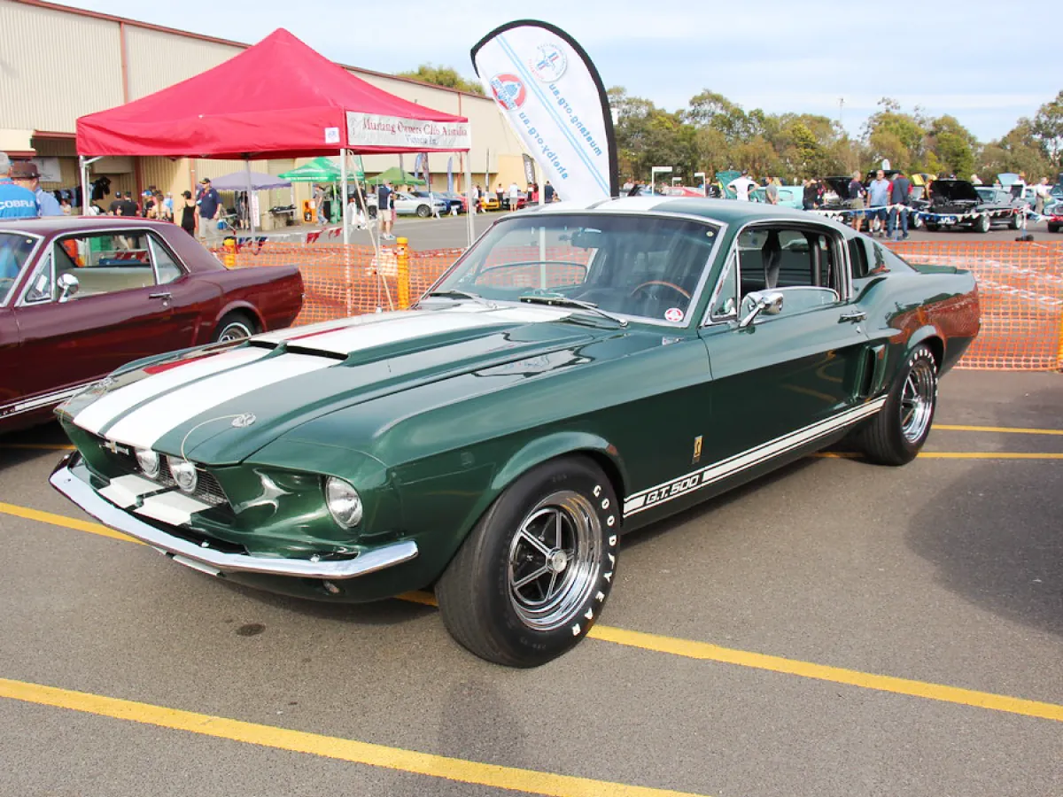 Ford Mustang Shelby GT500 (1967) na cor verde, estacionado em pátio ao lado de outros carros.