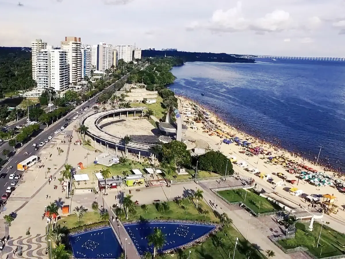 Orla do Complexo Turístico da Praia da Ponta Negra, com ampla infraestrutura, prédios de arquitetura variada e águas calmas do Rio Amazonas.