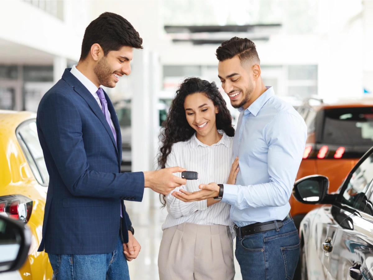 Casal, cliente de locadora, recebe de funcionário a chave de um carro alugado.