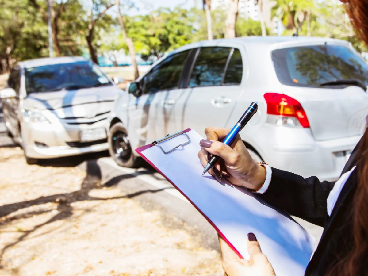 Dois carros parados frente a frente, enquanto pessoa anota, com caneta, algo numa folha sobre prancheta.