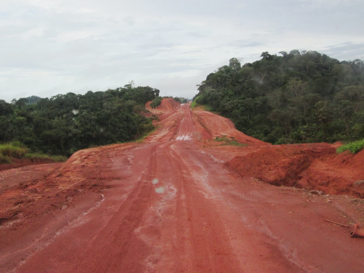 Trecho sem asfalto da BR-230, conhecida como Transamazônica. Terra vermelha protagoniza uma linha reta, enquanto a floresta mais famosa do mundo preenche os canteiros.