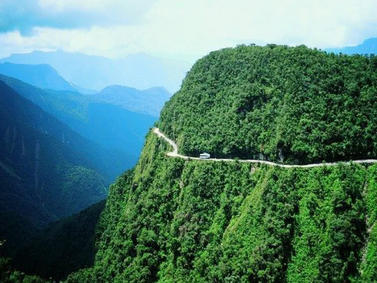 A imensidão das montanhas bolivianas e o Camino A Los Yungas, com mão única contornando penhascos cobertos por vegetação verde.