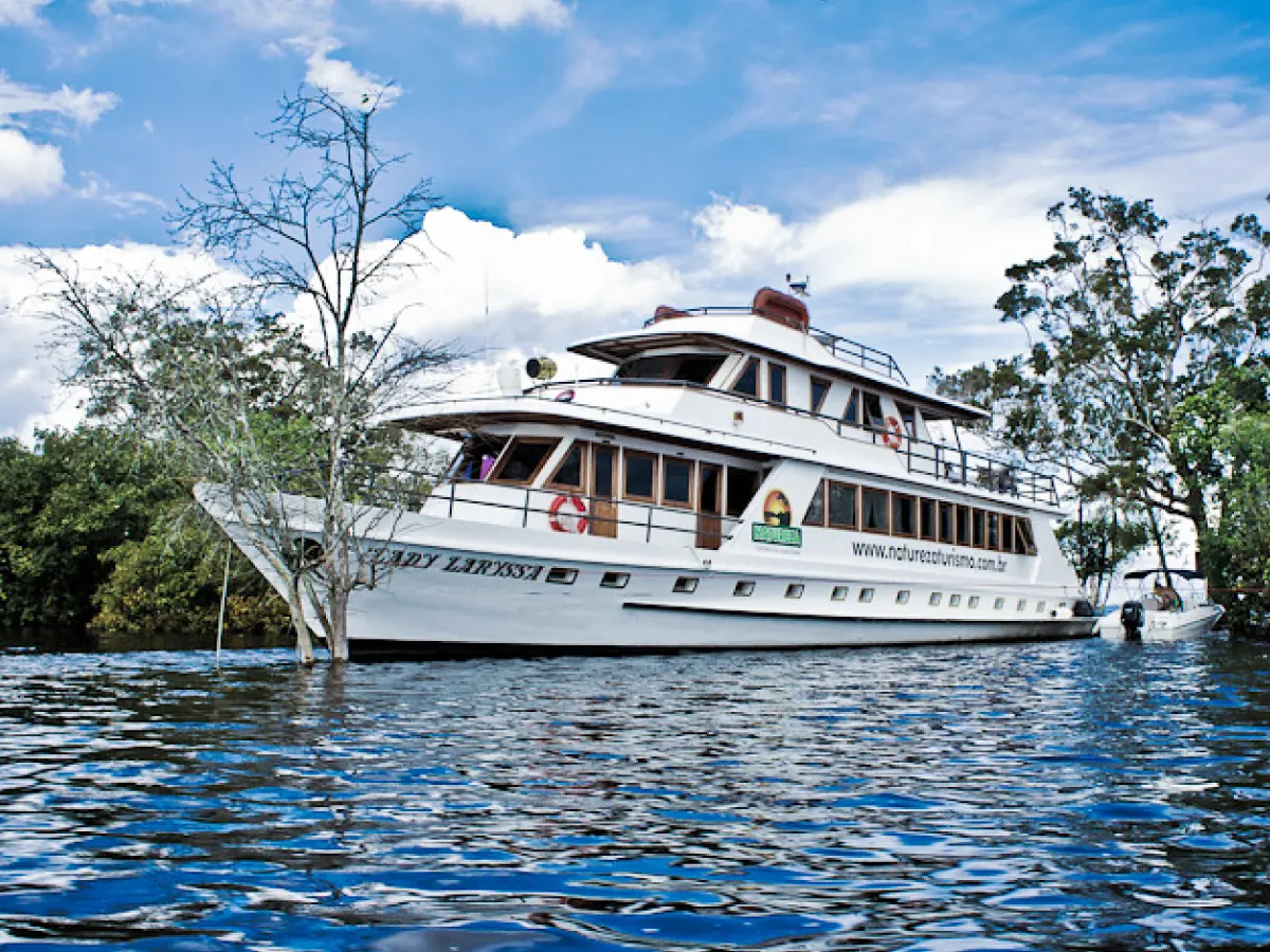 Embarcação de dois andares navega sobre igarapés da Praia do Tupé, com vegetação fluvial protagonizando a paisagem.