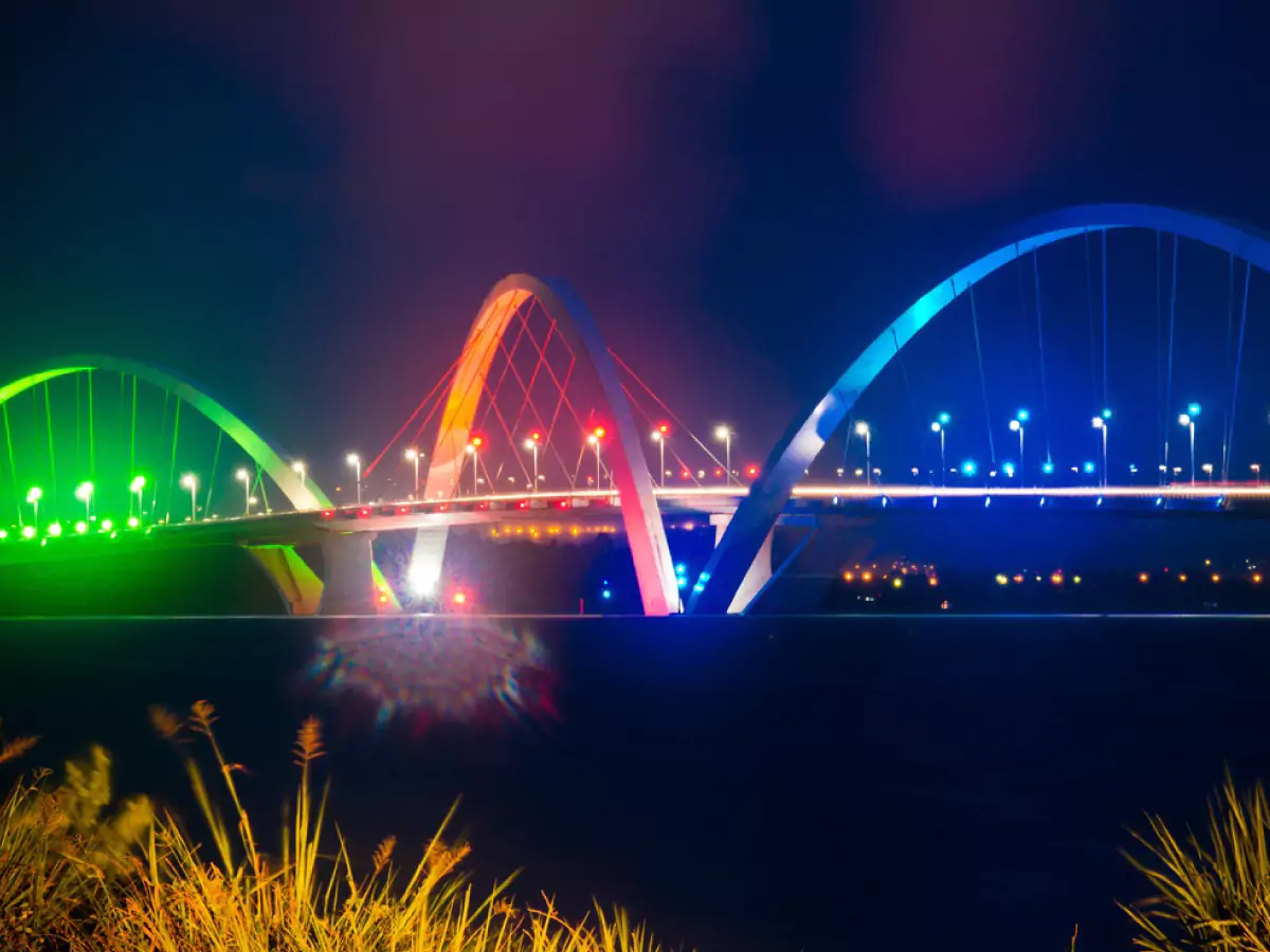 Ponte JK (Juscelino Kubitscheck) à noite, com suas luzes na cor verde, laranja e azul, imensa estrutura sobre o Lago Paranoá.