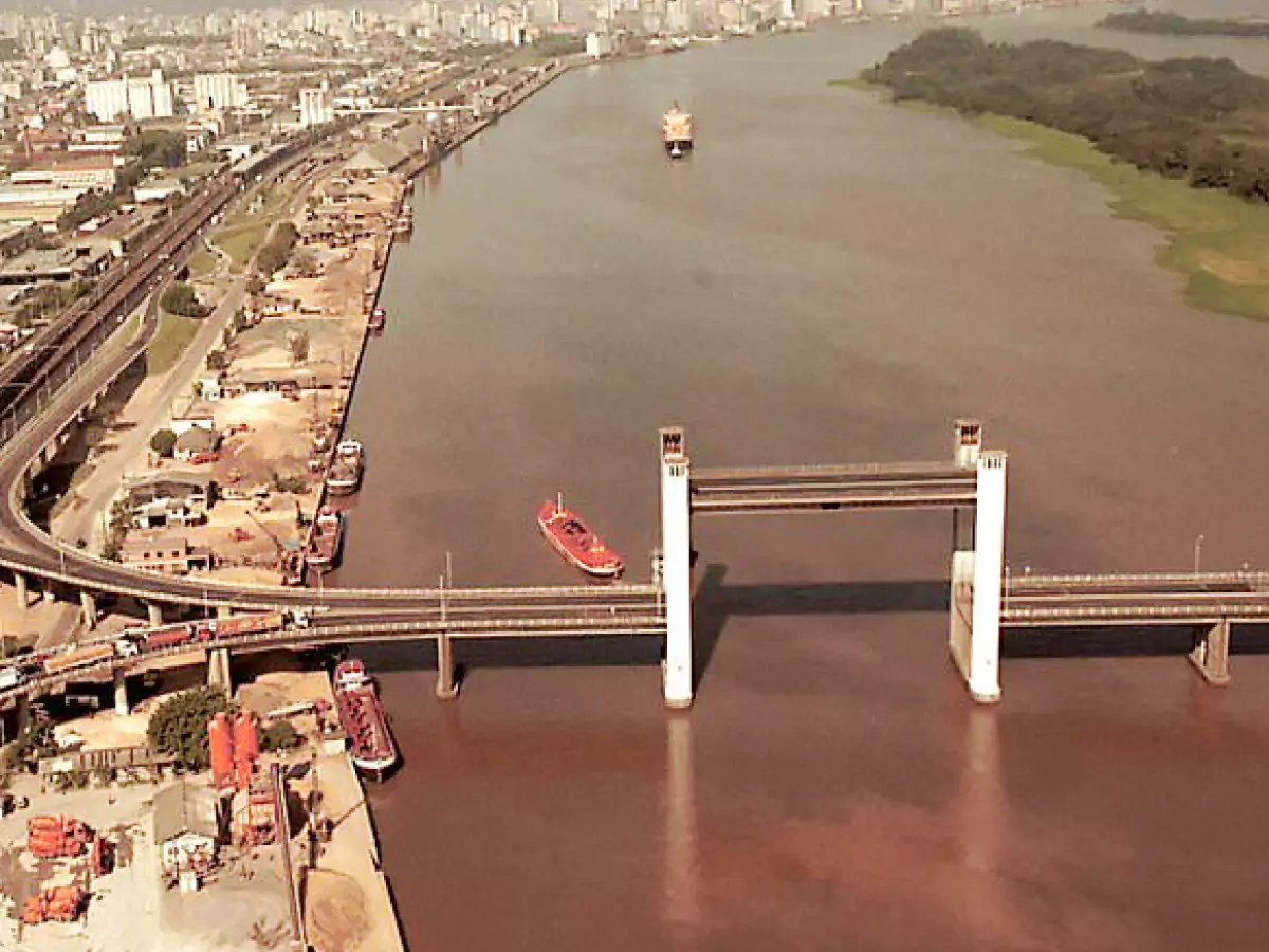 Ponte Getúlio Vargas, conhecida como Ponte Guaíba, com seu vão móvel erguido para que uma grande embarcação possa atravessar por baixo da estrutura. Há ainda outra embarcação ao fundo e no lado esquerdo uma pequena parte do porto, além de avenidas e prédios de Porto Alegre.