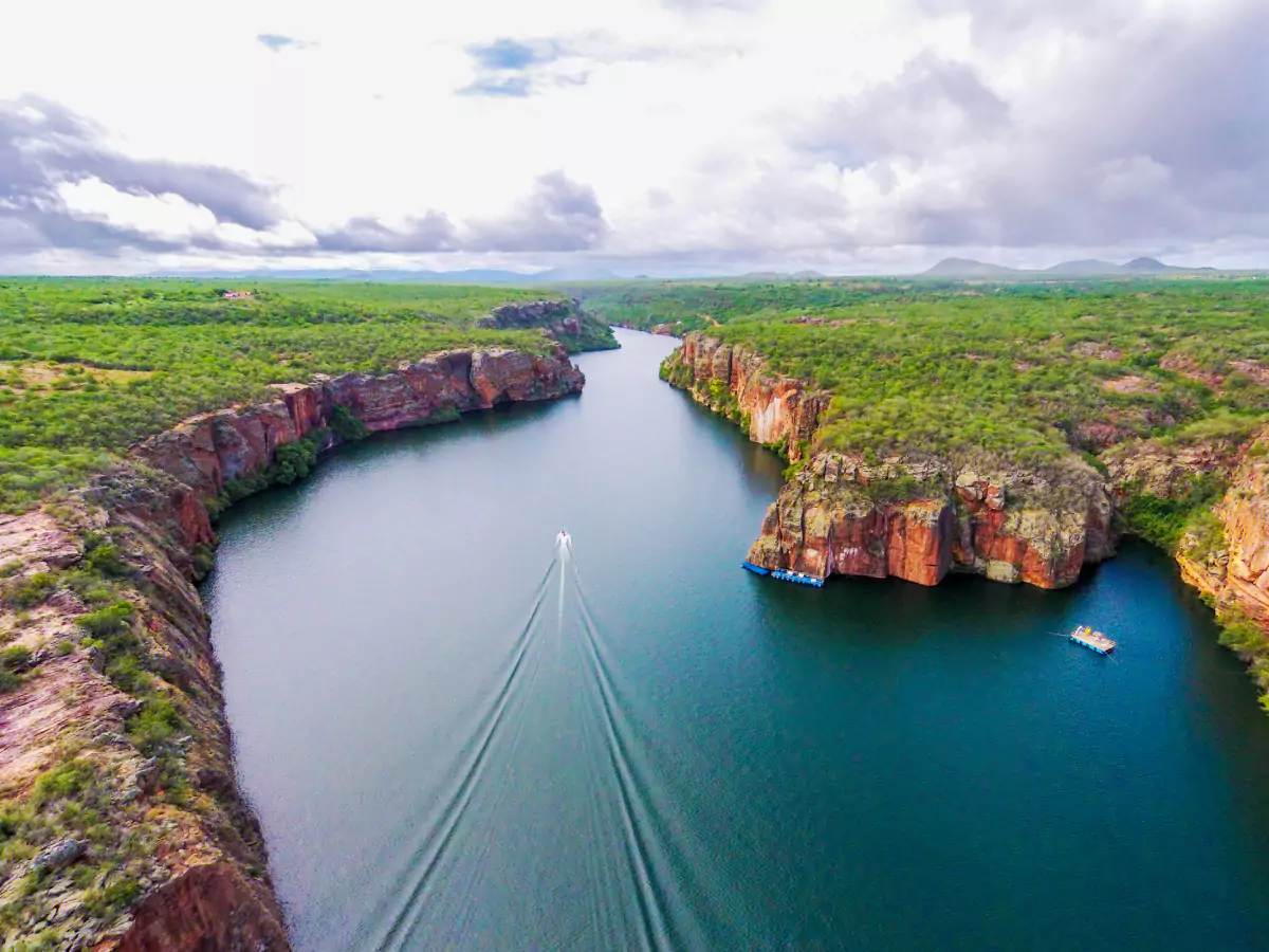 Extensão do Rio São Francisco, com seus paredões (cânios) contornando as margens e sobre eles diversas vegetações. No leito do rio há duas embarcações, uma parada e outra em pleno movimento.