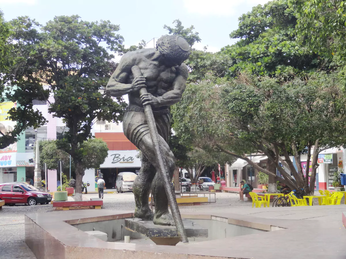 Praça São Tiago Maior, rodeada por árvores e comércios, dando destaque para a escultura de São Tiago.