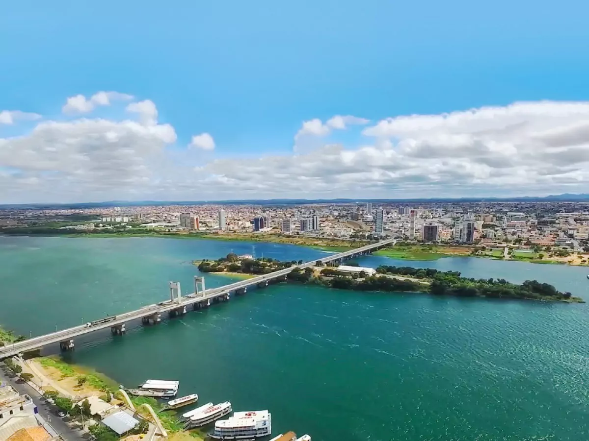 Ponte Presidente Dutra, que liga Juazeiro, na Bahia, a Petrolina, em Pernambuco. Sua estrutura atravessa o Rio São Franscisco. Na foto, ao fundo, uma das duas cidades segue em destaque. Às margens do Velho Chico há embarcações atracadas.