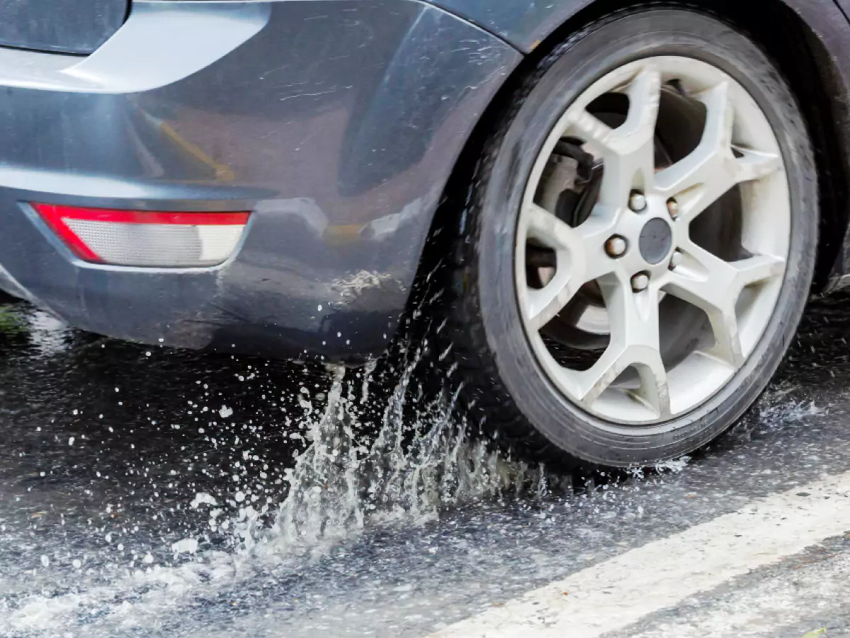 Roda de automóvel passa por cima de uma poça d'água, provocando aquaplanagem.