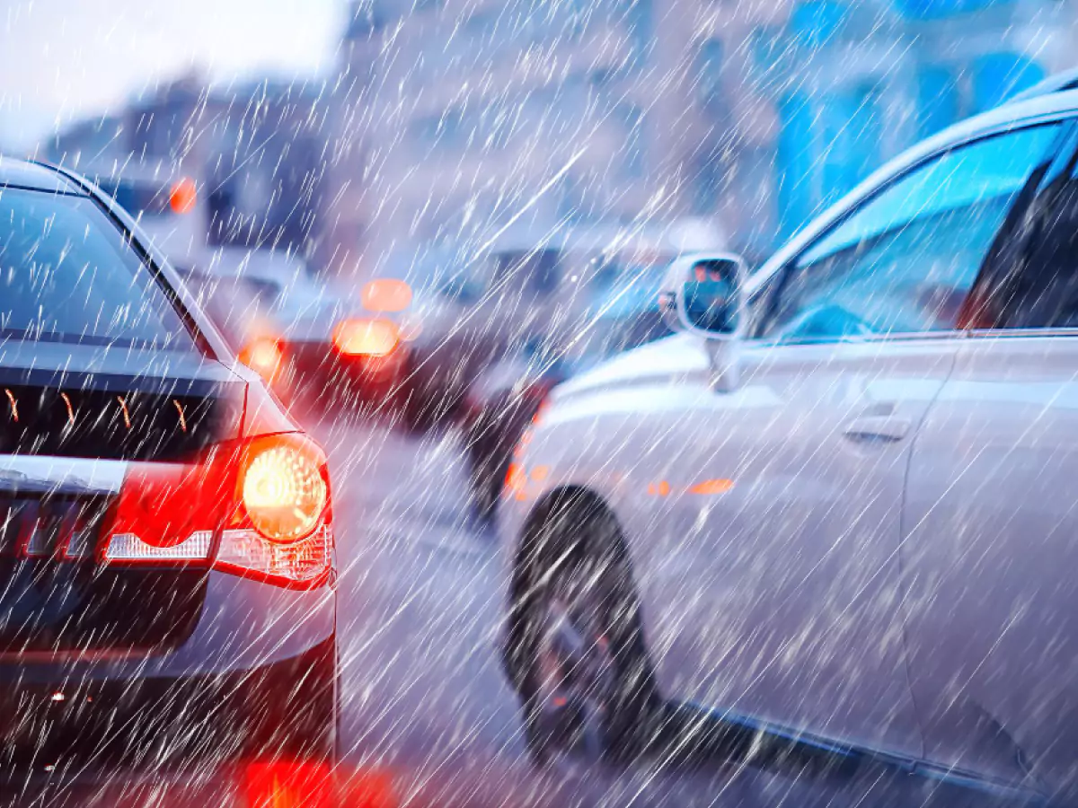 Dois carros em destaque trafegam na chuva. Detalhe no farol traseiro do carro preto, que está aceso.