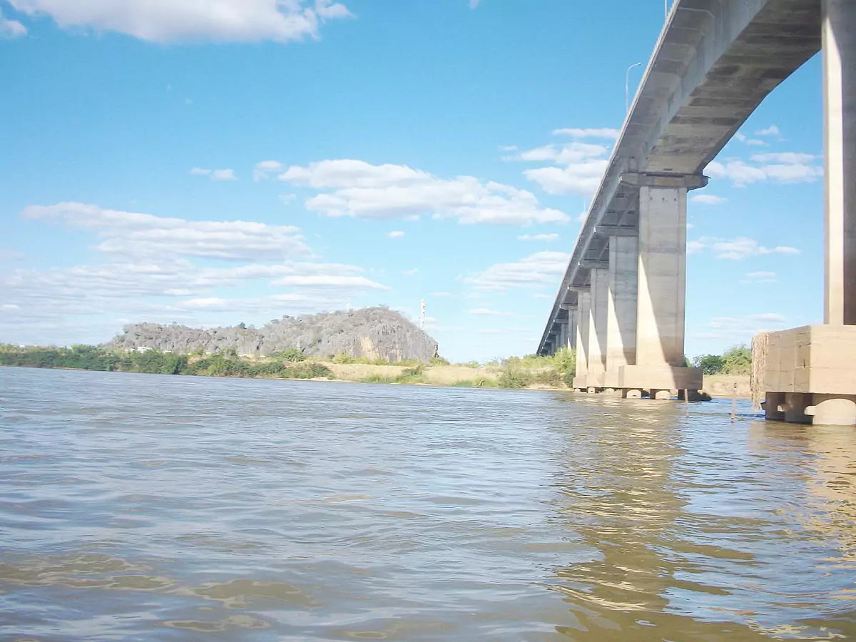 Estrutura da Ponte Gercino Coelho em destaque sobre o Rio São Francisco. Ao fundo há um morro. O céu encontra-se azul com formação de poucas nuvens.