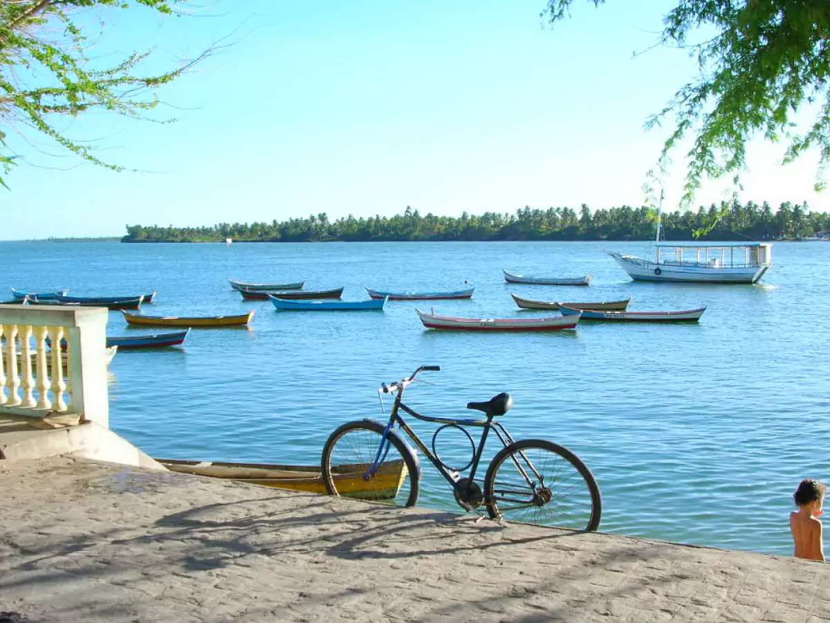 Bicicleta segue encostada em orla que margeia o Rio São Francisco, em Piaçabuçu (Alagoas). Há embarcações atracadas. As águas do rio competem na cor azulada com o céu sem nuvens.