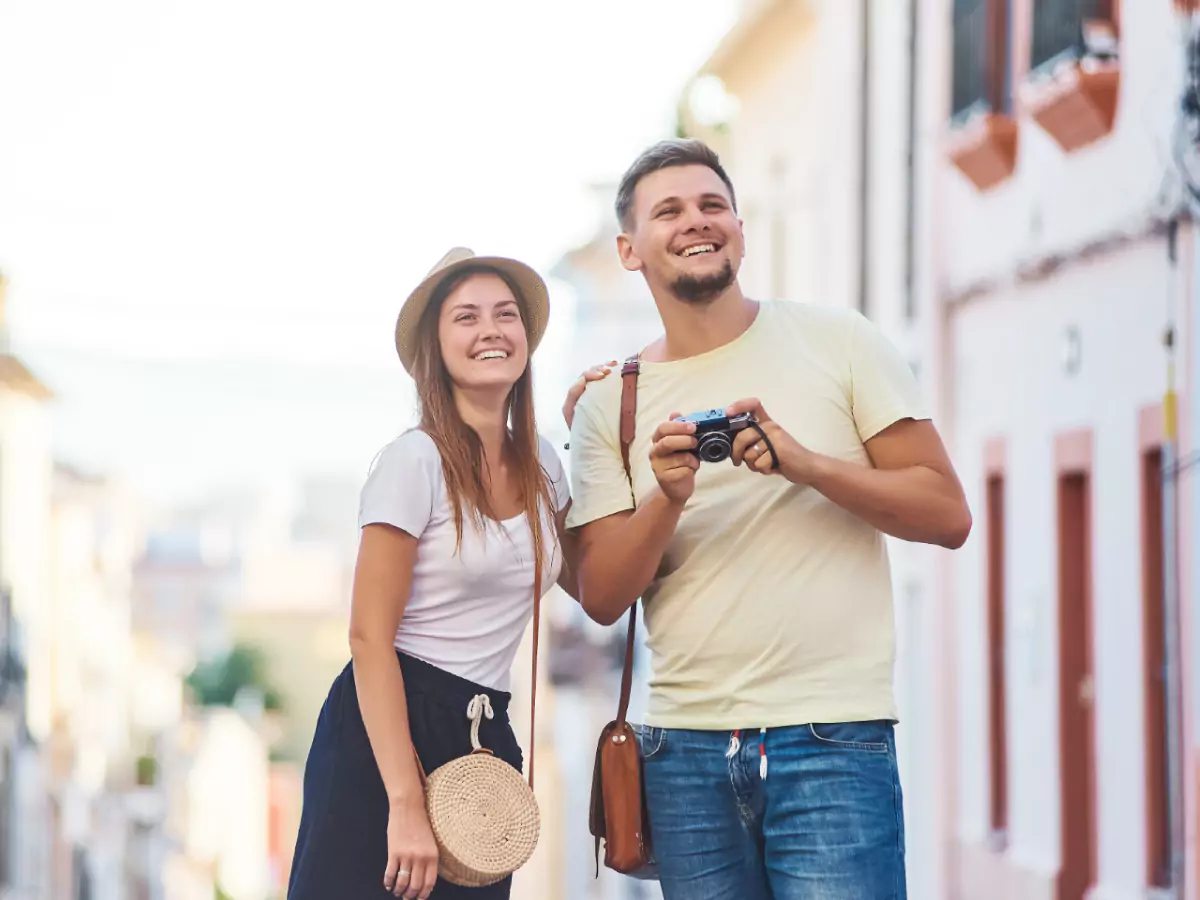 Casal em ladeira de cidade turística do Rio São Francisco. Tanto o rapaz quanto a moça portam, cada qual, uma bolsa. Ele segura uma máquina fotográfica preparando um clique.