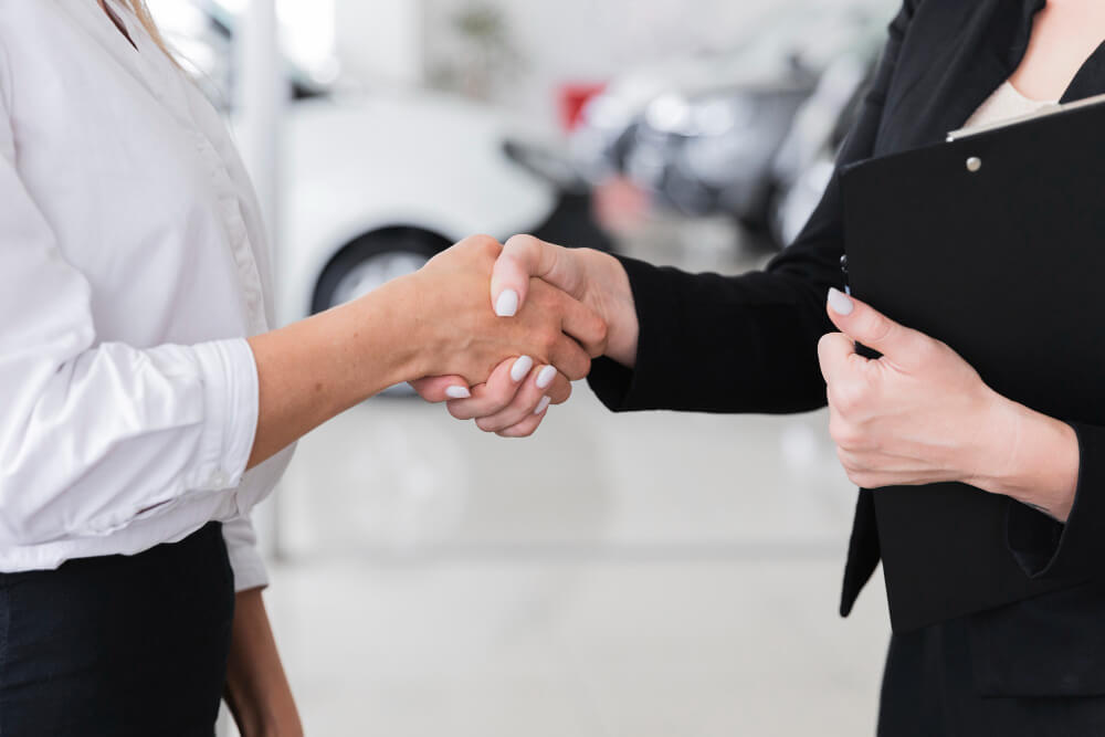 Em uma loja de carros, duas mulheres fecham negócio por meio de um aperto de mãos