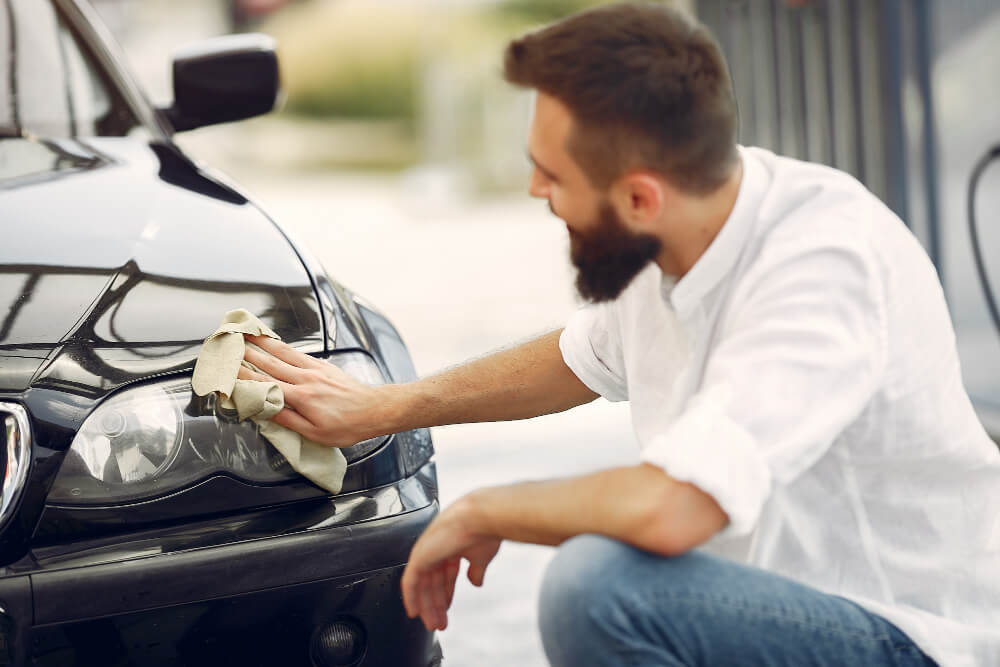 Homem de camisa branca limpa um carro em uma lavandaria